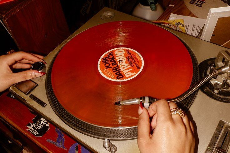 Disco de vinilo rojo girando en un tocadiscos, con dos manos sobre la aguja