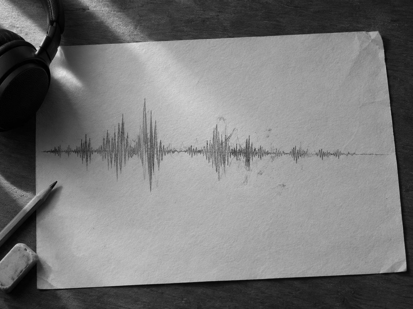 Forma de onda de audio dibujada a lápiz sobre papel crema, con un trazo naranja, junto a unos audífonos, un lápiz y una goma